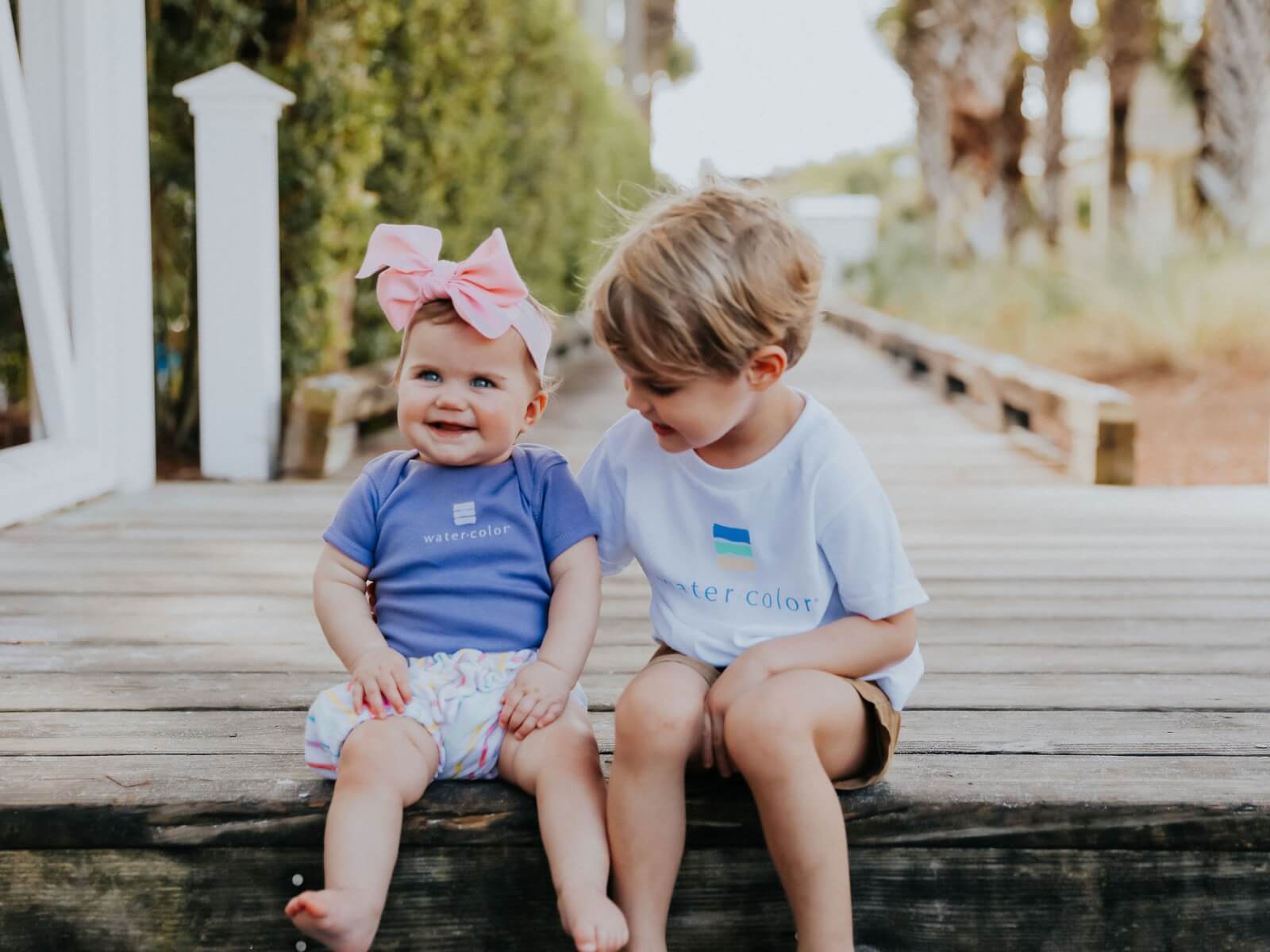 Two children sitting on a wooden deck.