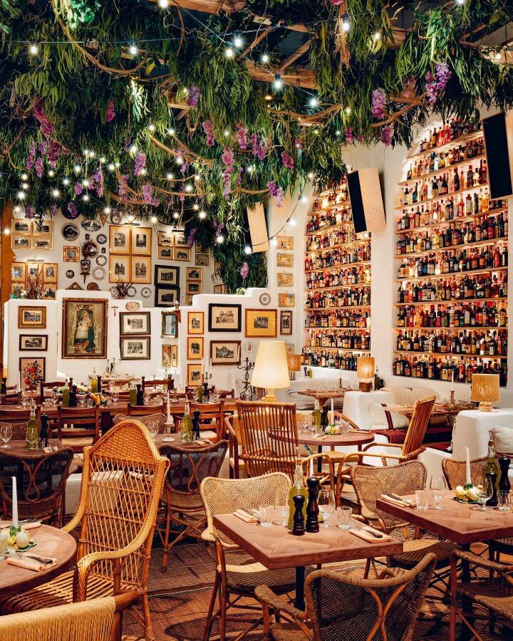 Decorative restaurant interior with greenery, framed pictures, and a colorful bar invites you to enjoy a cozy long weekend in London. Wooden tables and chairs are perfectly set for dining.