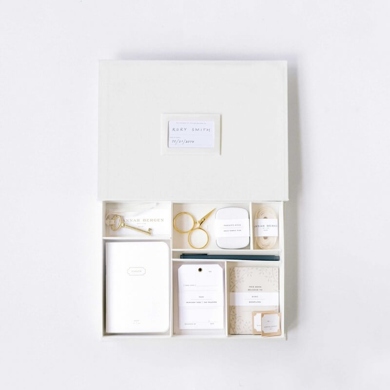 A neatly organized white box with scissors, cards, notebooks, and labels rests on a crisp white background