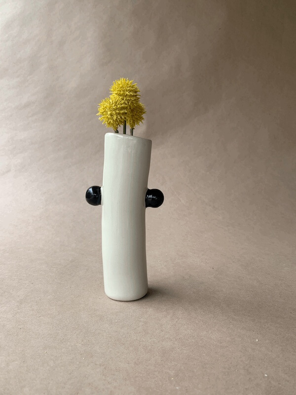 Modern white vase with two black handles cradles vibrant yellow pom-pom flowers against a plain backdrop.