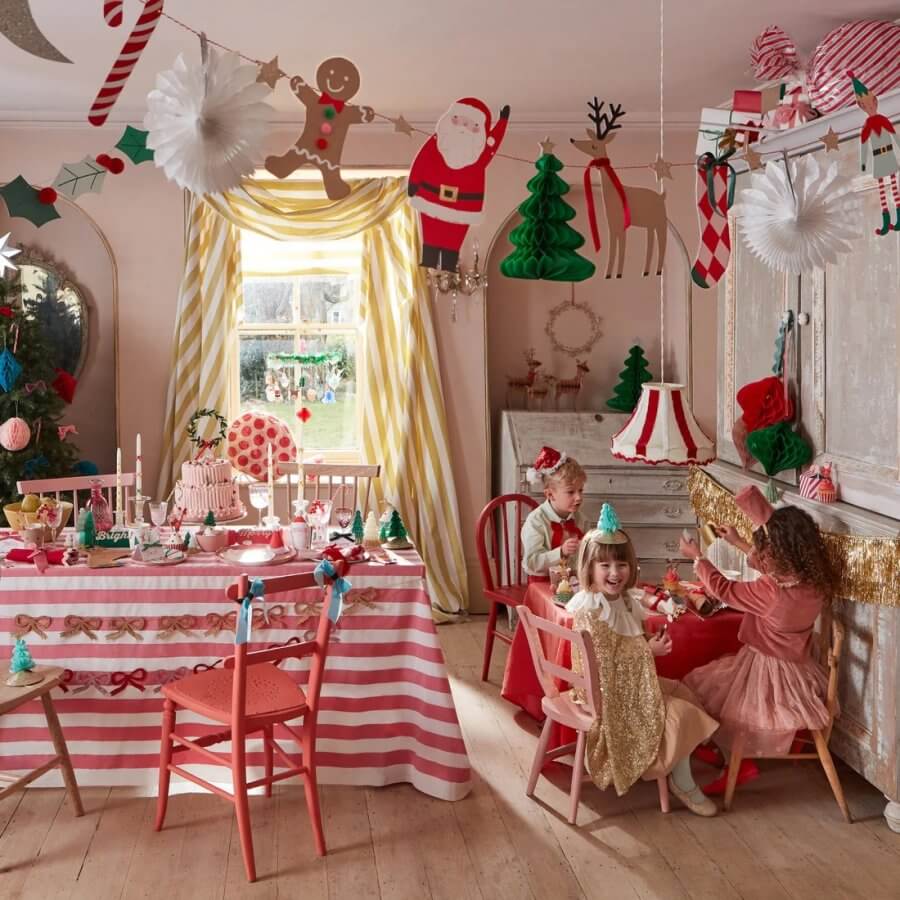 The festive room, adorned with holiday decorations and joyful children playing, showcases a beautifully set table for the Christmas party. 