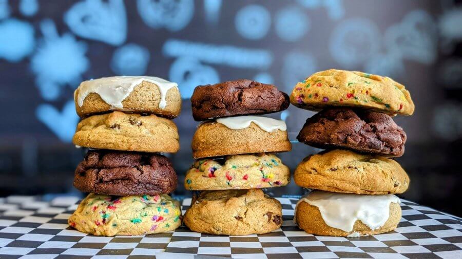 Three stacks of assorted cookies, crafted by cookie companies that ship, feature icing, including chocolate, sprinkle, and plain varieties. They rest on a checkered surface with a blurred background.