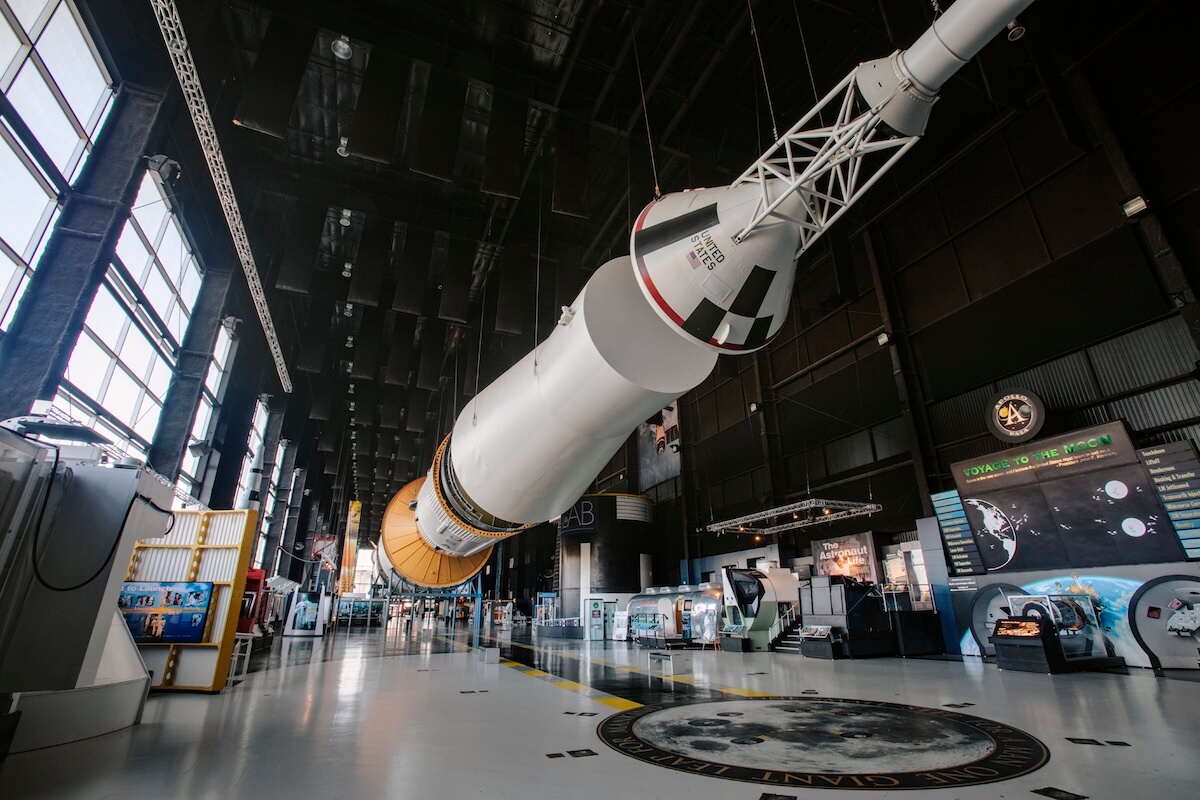 A large Saturn V rocket is displayed horizontally inside a spacious museum hall in one of the best towns to visit in Alabama, surrounded by exhibition panels and educational displays.