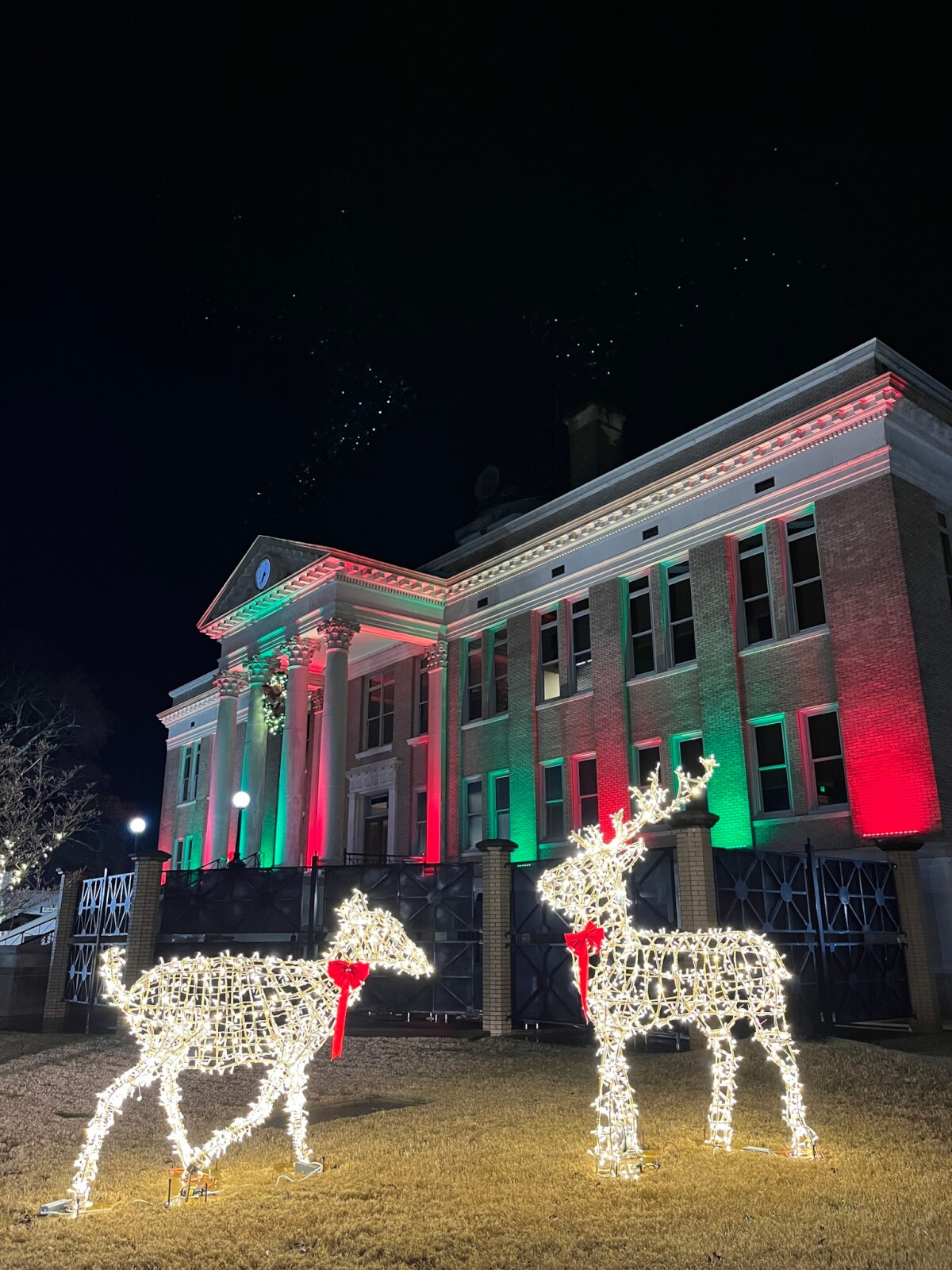 Two illuminated reindeer figures stand in front of an Alabama building lit with red and green lights at night, making it a charming holiday destination.