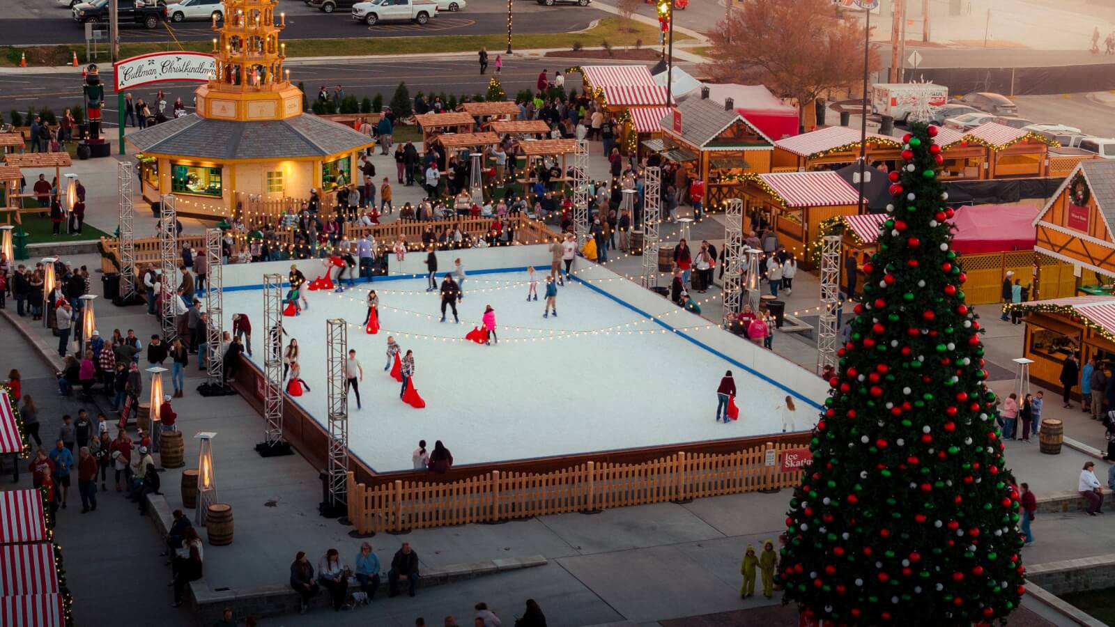 Aerial view of an outdoor ice skating rink surrounded by people and festive market stalls, with a large decorated Christmas tree nearby, capturing the charm of holiday destinations. This scene brings festive cheer to even unexpected places like Alabama.