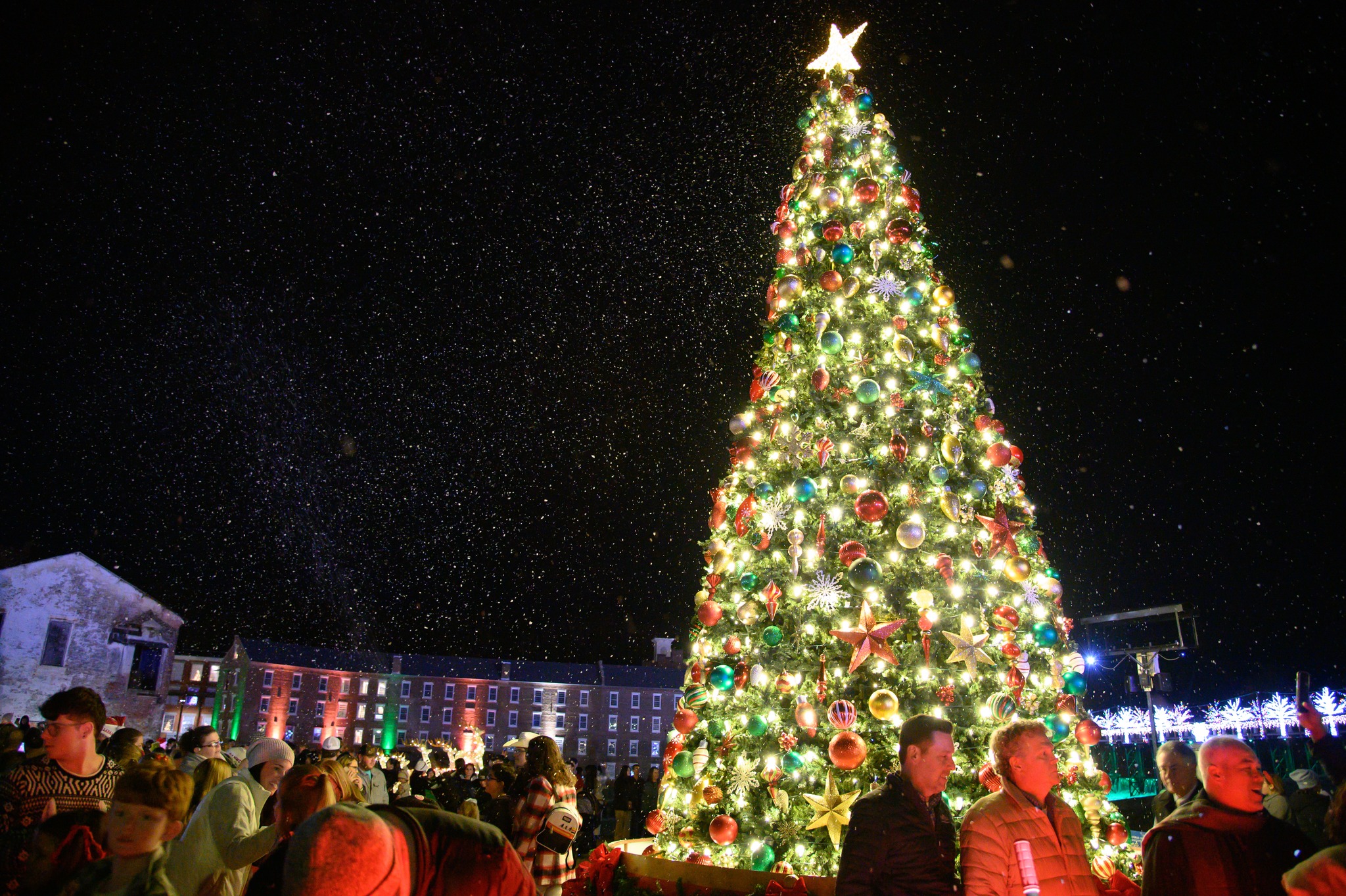 A large, decorated Christmas tree with lights and ornaments stands in a public square at night, surrounded by people, making Alabama a magical holiday destination.