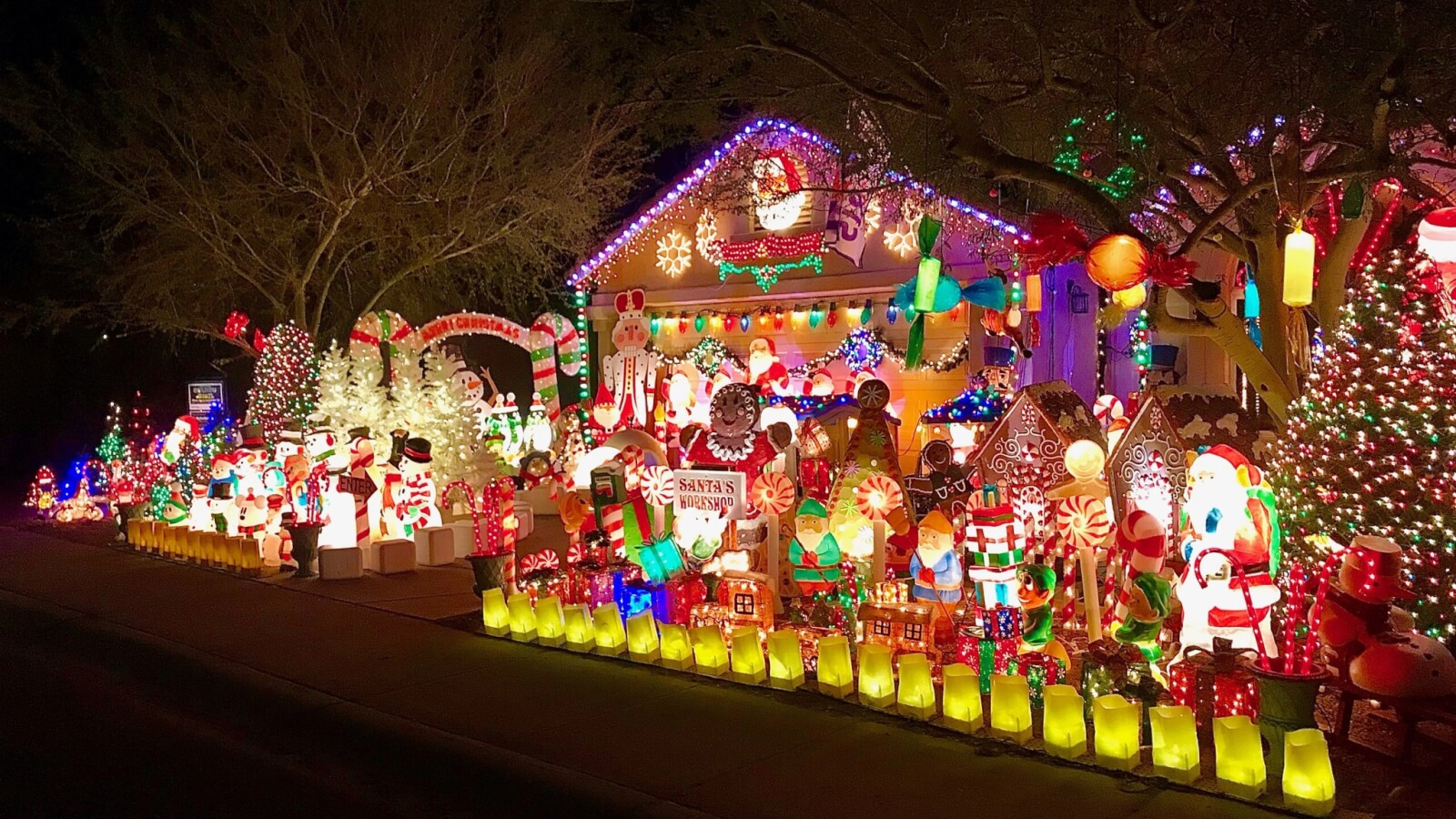 A house in Alabama is brightly decorated with numerous colorful Christmas lights and inflatable holiday figures, including Santa Claus and snowmen, creating a festive display at night. 