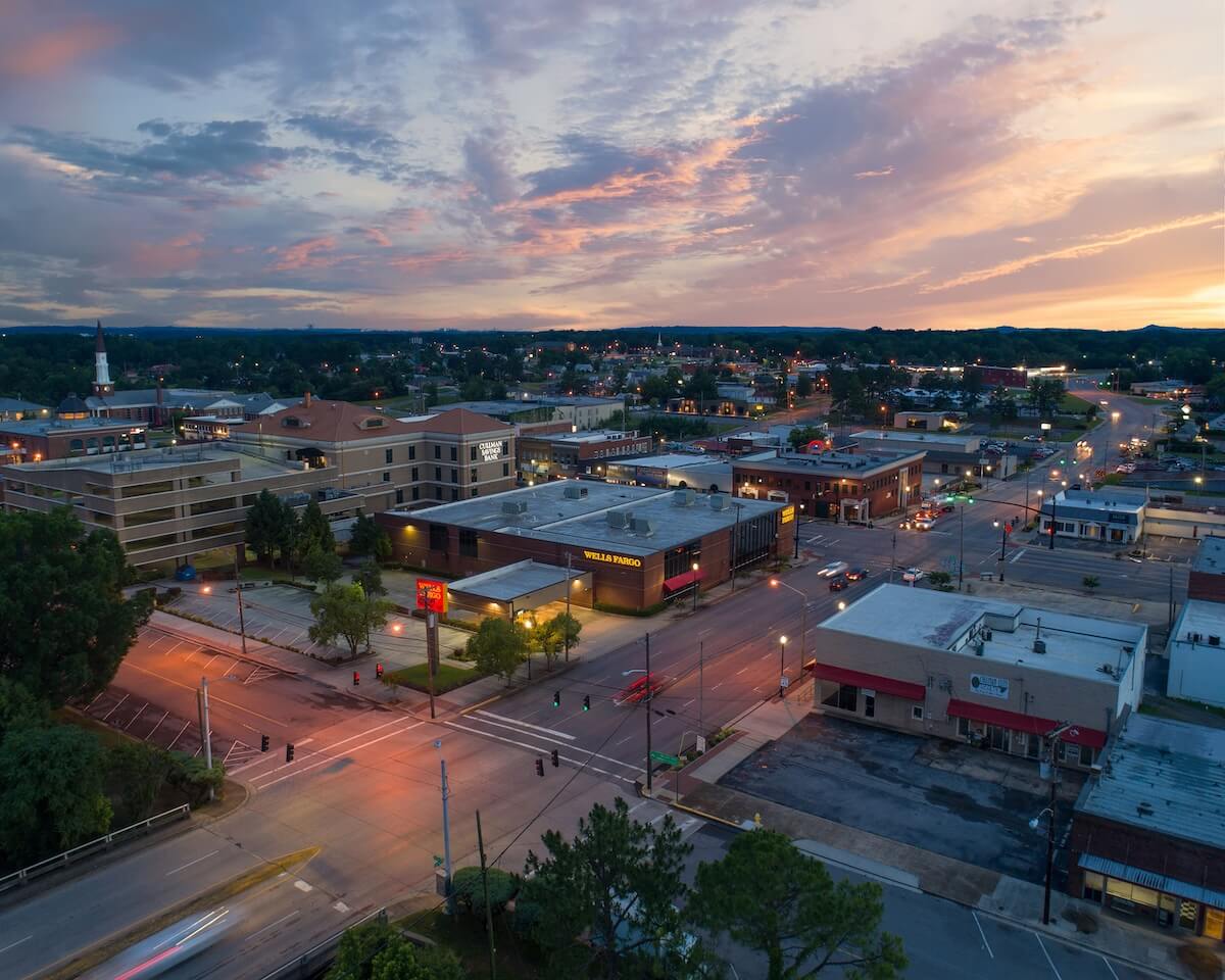 Aerial view of a small town at sunset, featuring roads, buildings, and scattered streetlights.