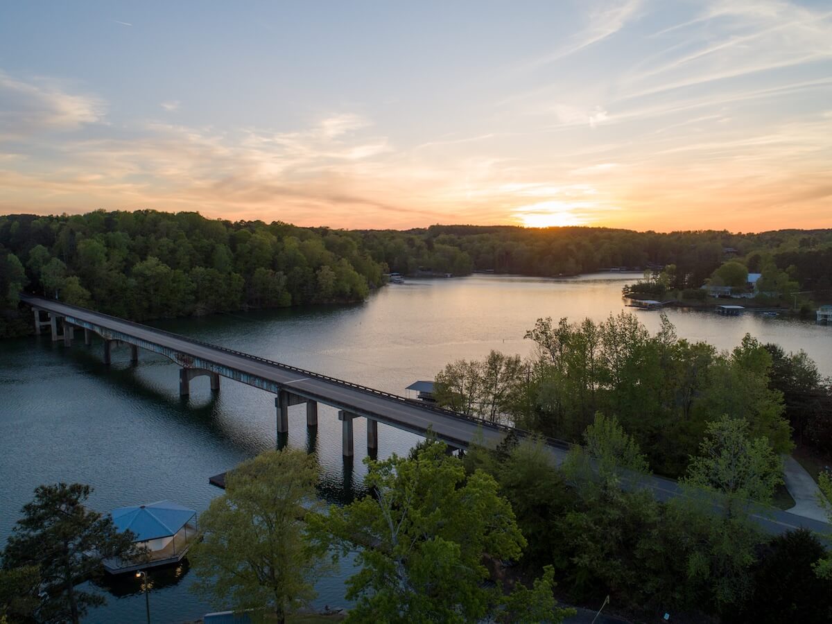 Sunset view over a tranquil lake with a long bridge and surrounding greenery.