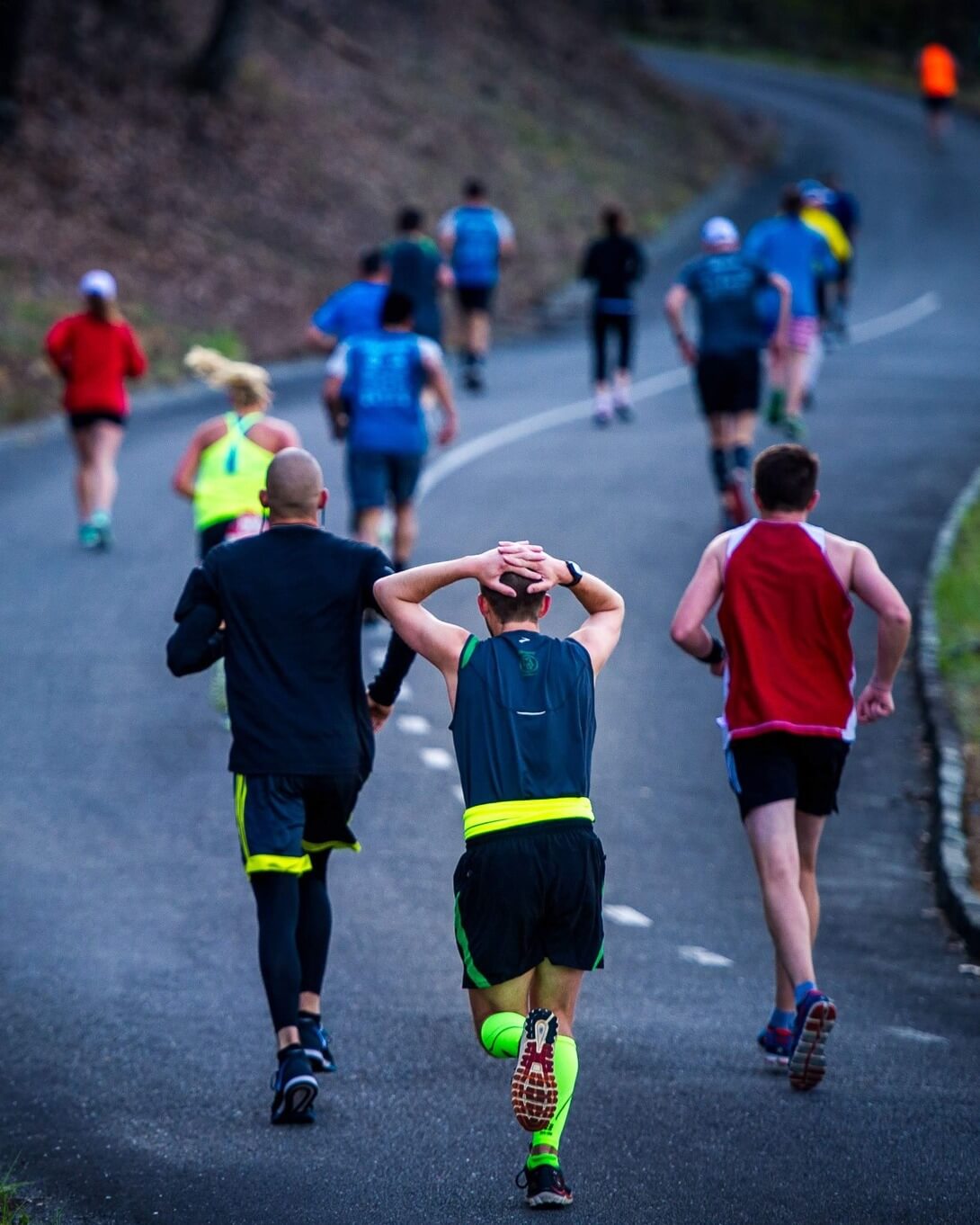 A group of runners hits the road in vibrant athletic gear, with trees lining their path. Neon accents catch the eye as they tackle one of the best spring marathons, while a runner holds his head