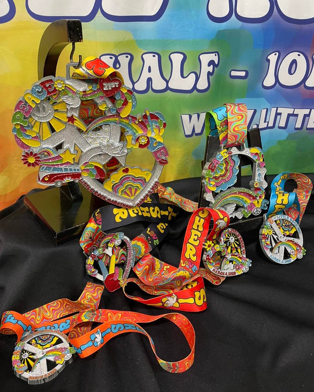 Colorful medals and ribbons with peace and floral designs are displayed on a black cloth. The backdrop features partial text in bold colors.