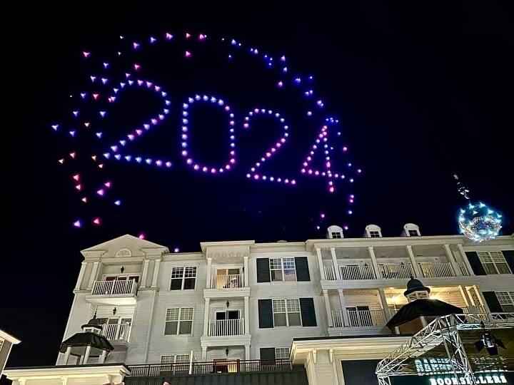 Drones form "2024" in the night sky above a building, their blue and purple lights creating a circular pattern as part of the New Year's Eve countdown.