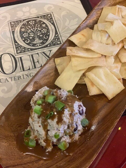 A rustic wooden platter showcases crispy pita bread slices accompanied by a velvety, sauce-drizzled dip garnished with fresh green onions. 