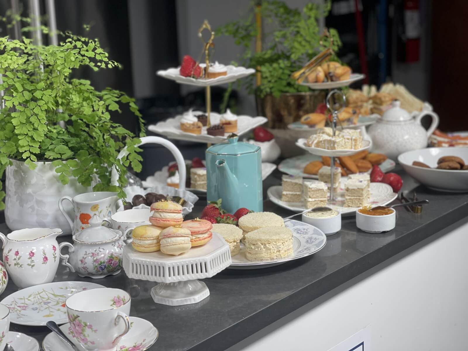 An elegant afternoon tea setup features an array of pastries, sandwiches, and macarons set gracefully alongside intricately designed tea cups on the table.