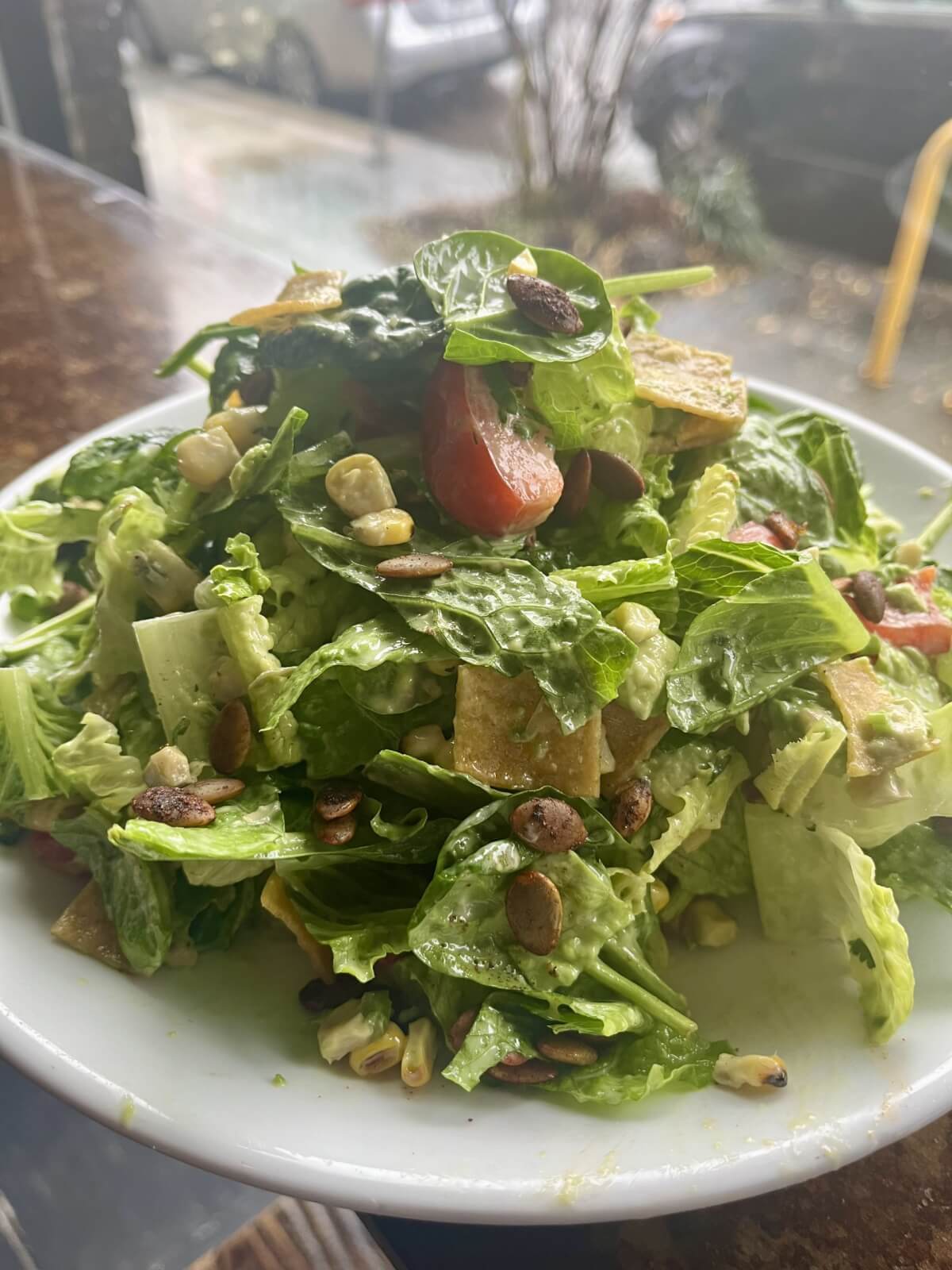 Discover one of Birmingham's best salads—a vibrant mix of lettuce, tomato, corn, avocado, and pumpkin seeds artfully served on a white plate.