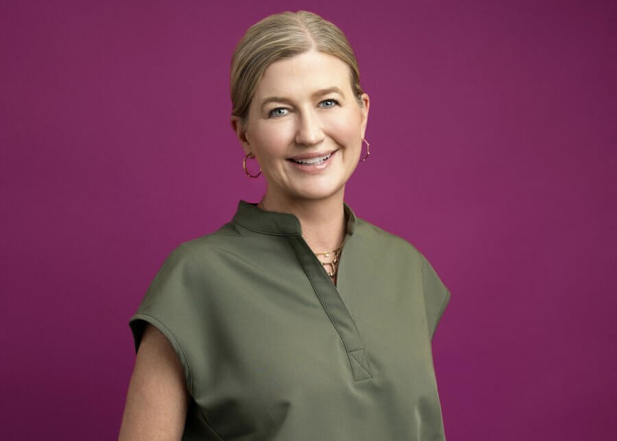 Dr. Jenny Sobera, in green scrubs with hoop earrings, smiles warmly against a magenta background