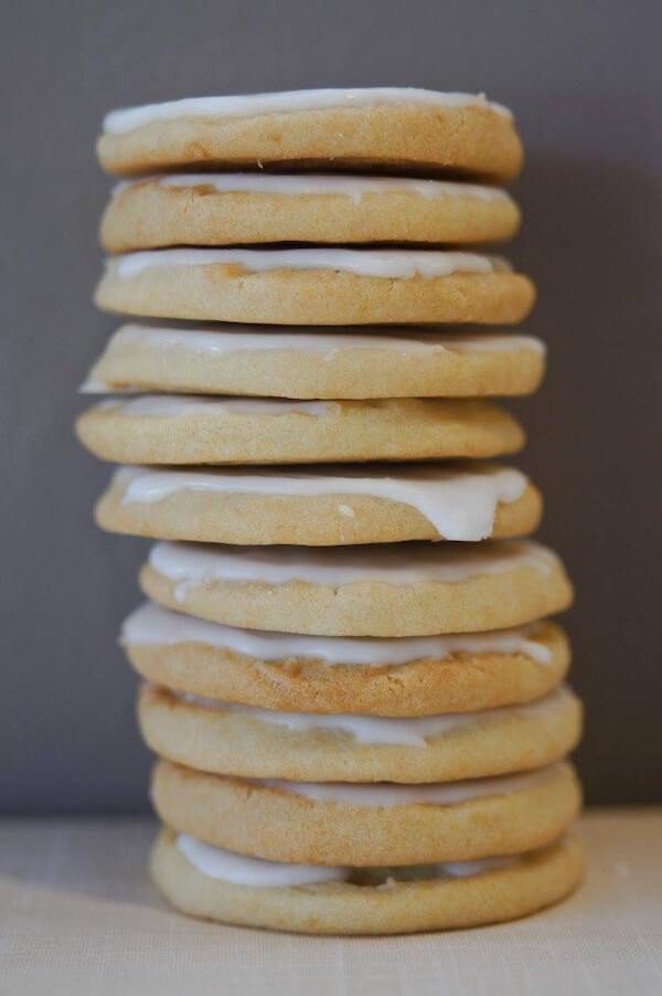 A stack of eleven round sugar cookies with white icing between each layer, placed on a neutral background, showcases the delightful creations from cookie companies that ship.