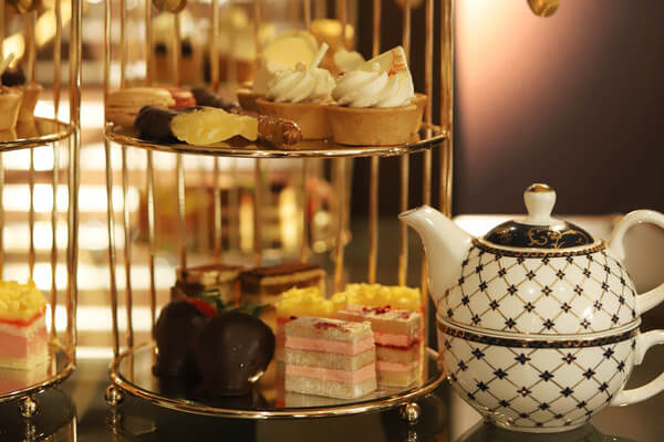 A decorative teapot sits alongside a multi-tiered stand with assorted pastries, including tarts, macarons, and layered cakes—all elegantly presented for a Chocolate Affair.