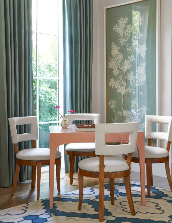 White dining room chairs surrounding a pink table in a teal-colored room.