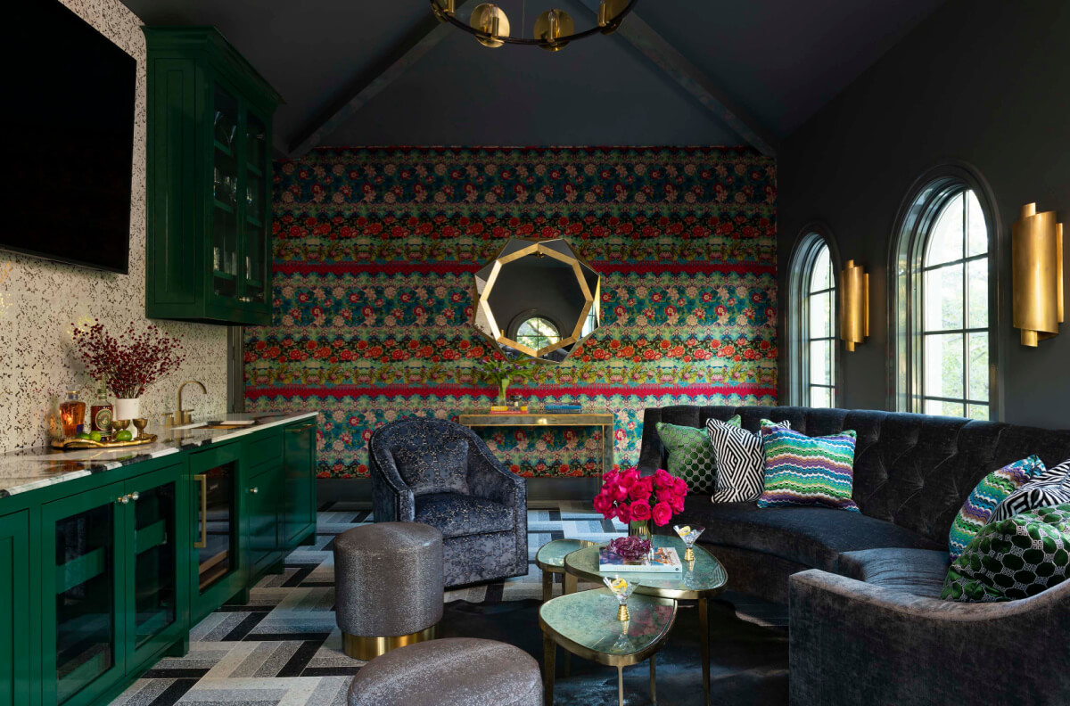 A stylish living room featuring 2025 interior design trends with dark green cabinetry, patterned wallpaper, a gray curved sofa, round cushioned chairs, a geometric rug, flowers on glass tables, and arched windows.