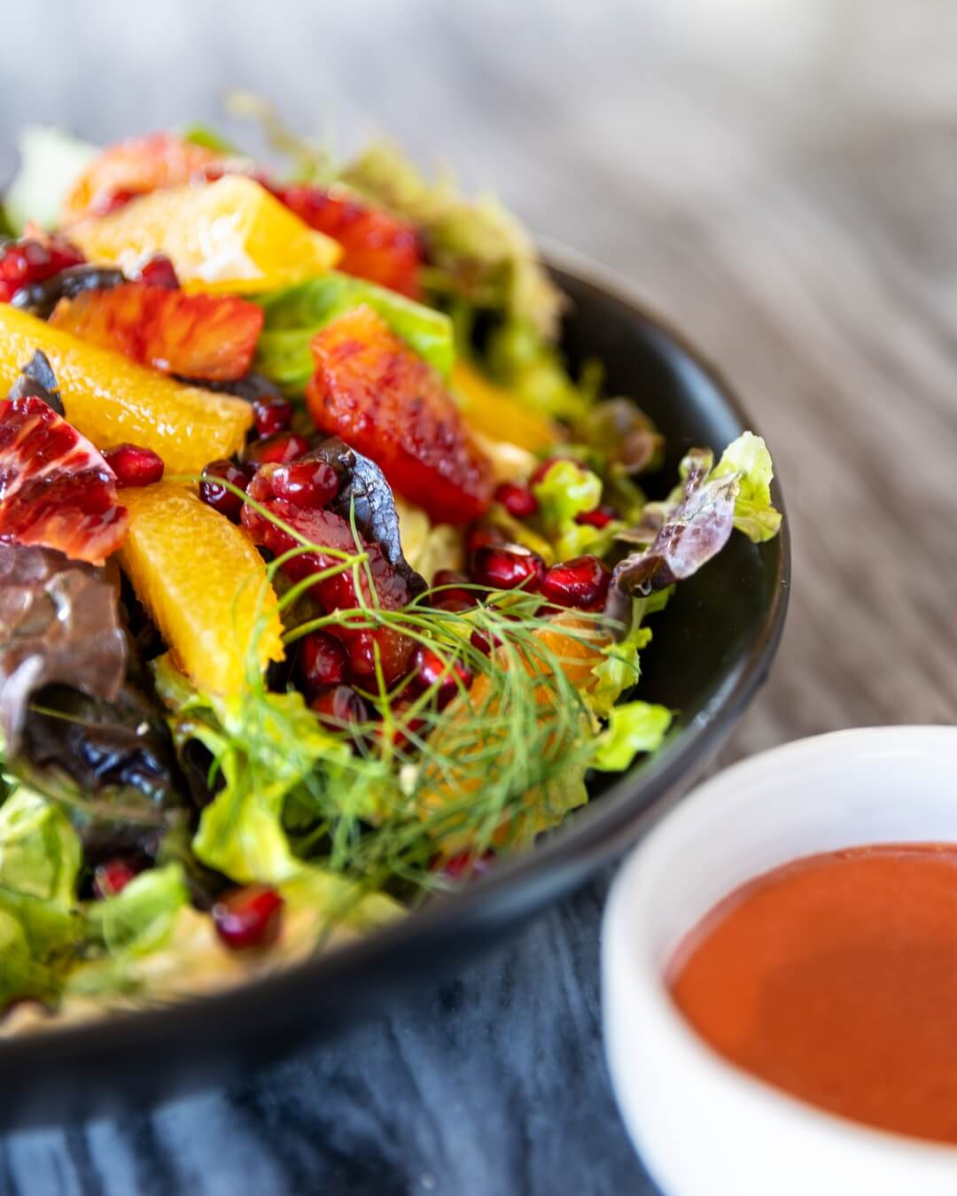 salad on a black plate next to a cup of dressing