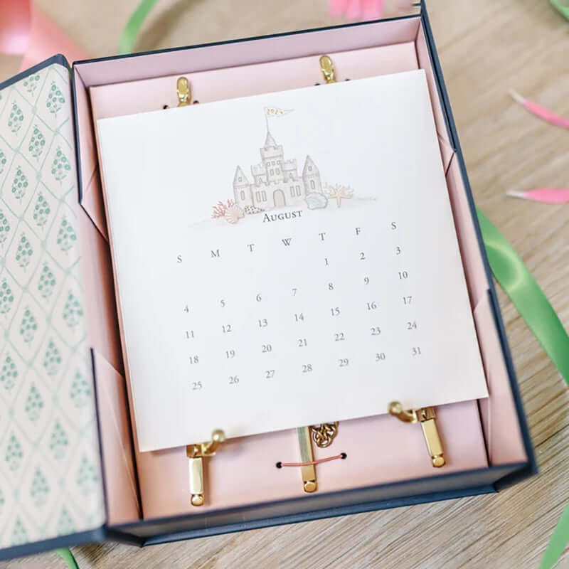 A decorative calendar featuring August and an illustration of a castle rests open in a patterned box, evoking the artistic spirit of Memphis.