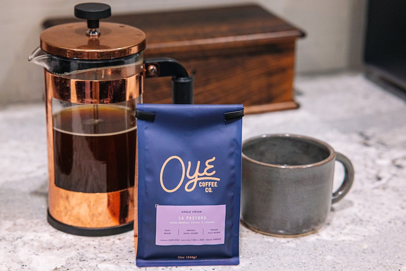 On the countertop sits a French press, a mug, and a bag of Oye Coffee Co. La Pastora coffee.