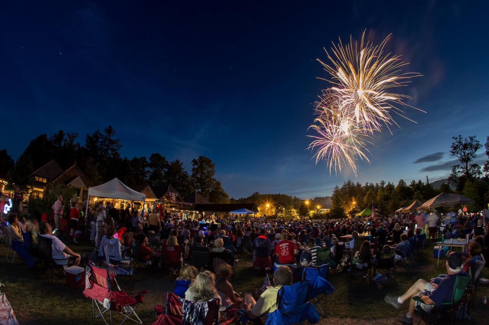 Fireworks going off over a field of people sitting in lawn chairs.