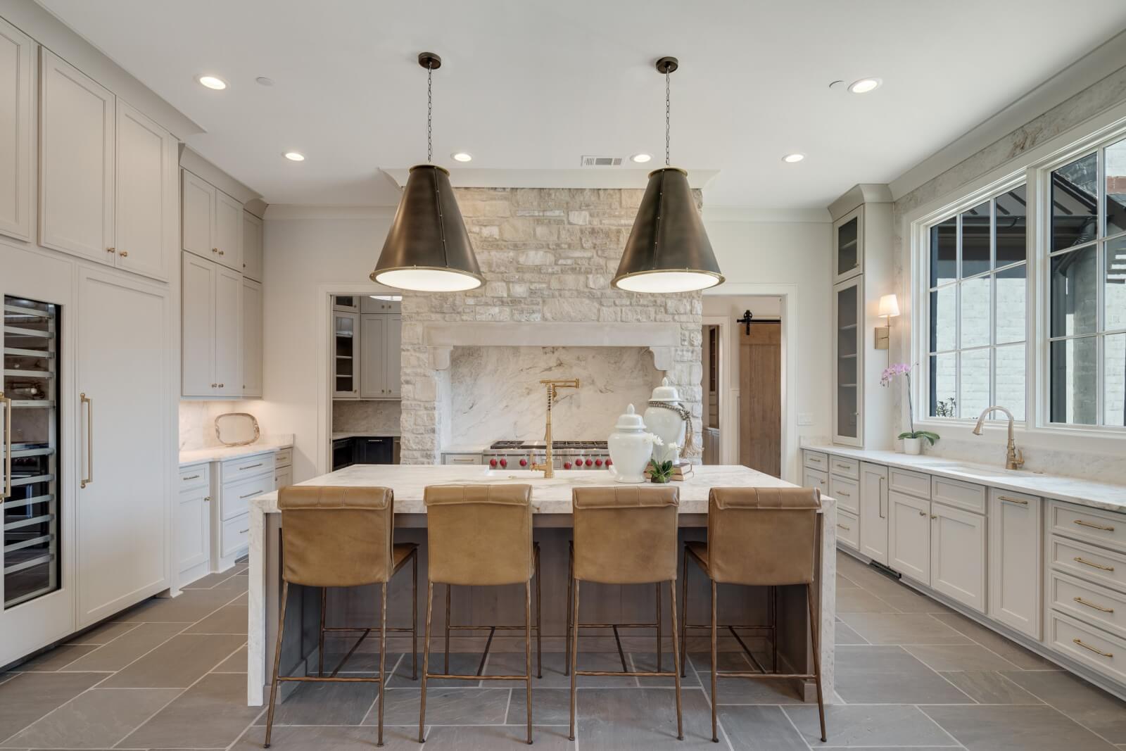 Spacious kitchen with natural stone backsplash, large island, and leather barstools. Incorporates pendant lights, stainless steel appliances, and big windows to create a welcoming home atmosphere.