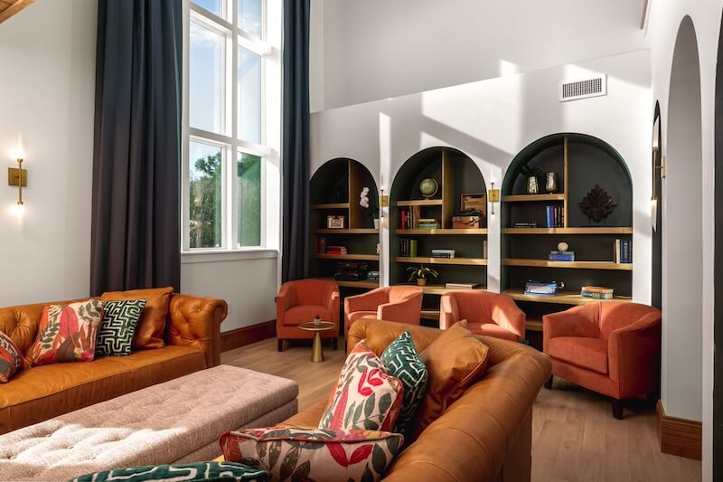 A stylish living room with terracotta sofas, patterned cushions, arched bookshelves inspired by 30a hotels, and sunlit windows.