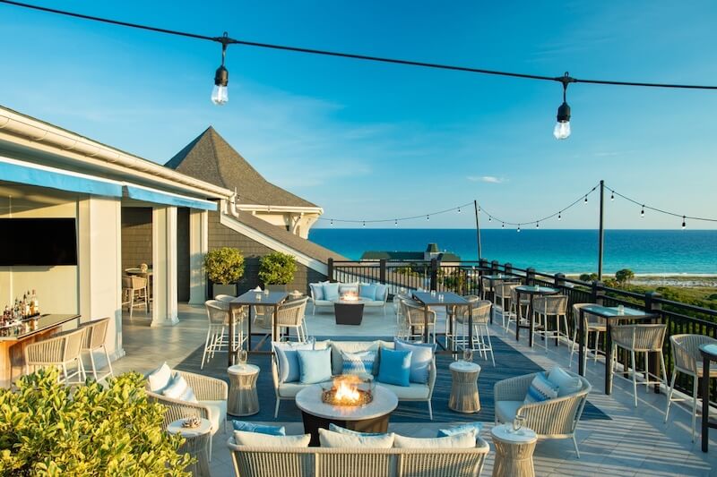 Oceanfront terrace with fire pit, string lights, and seating area overlooking the beach at one of the 30a hotels during daytime.