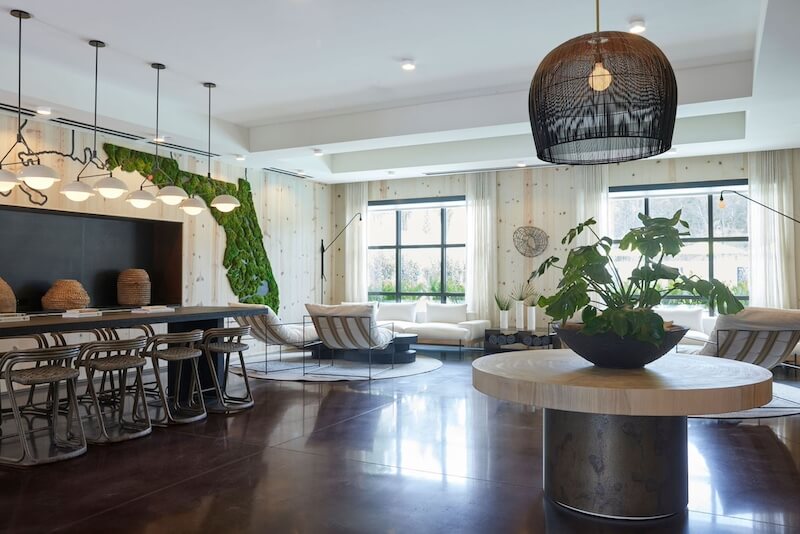 Modern, spacious hotel living room with a kitchen bar, large windows, hanging lamps, and a blend of cozy and stylish furniture.