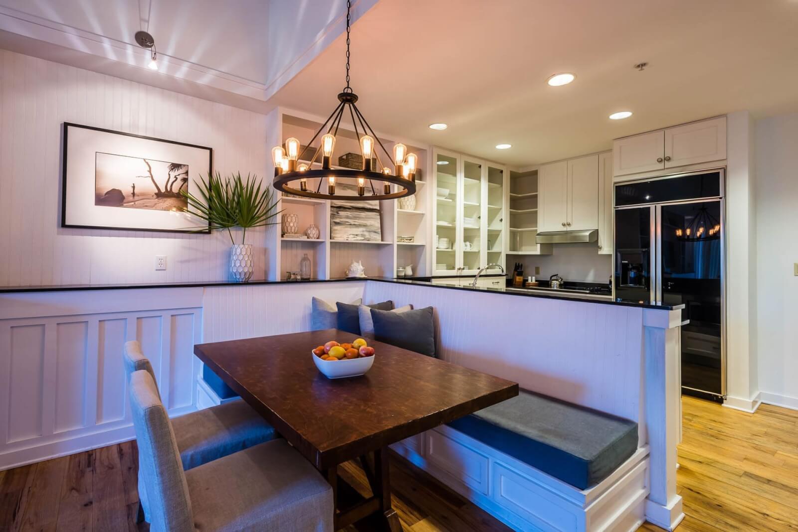 Modern kitchen with white cabinetry and built-in dining nook featuring a wooden table framed by pendant lighting, resembling the elegant design found in 30a hotels.