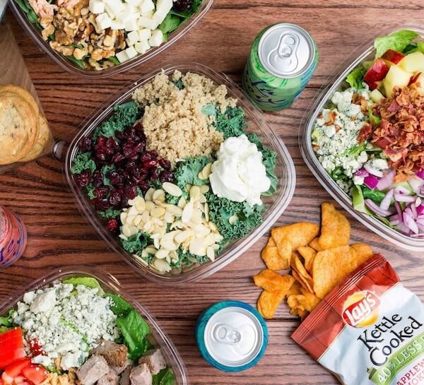 A table displays an array of the best salads in Memphis, accompanied by cans of sparkling water, a pack of Lay's chips, and cookies.