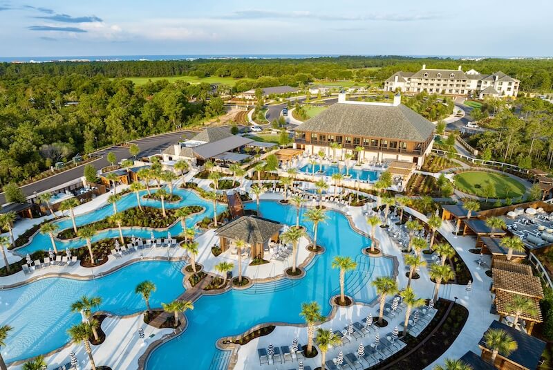 Aerial view of a 30a hotel luxury resort with expansive swimming pools and sun loungers surrounded by lush greenery.