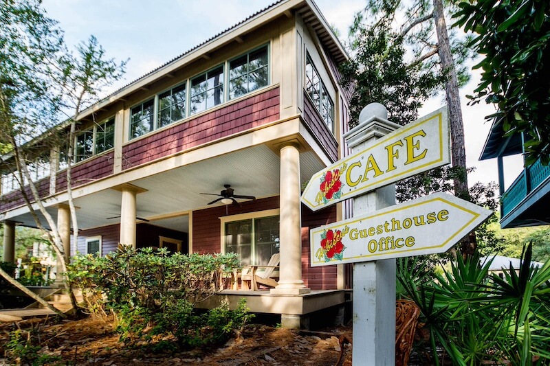 Café and guesthouse office sign outside a two-story 30a hotels building with a porch and surrounded by trees.