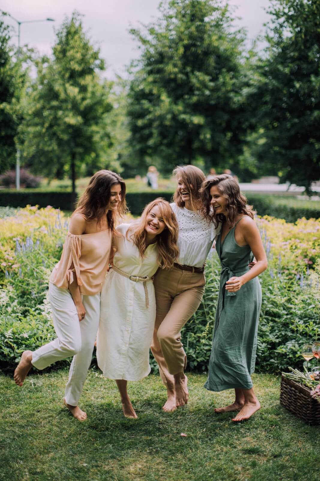 Four women, embodying the spirit of Blue Zones, are laughing and walking in a garden with green trees and bushes in the background, embracing the joy of healthier lives.