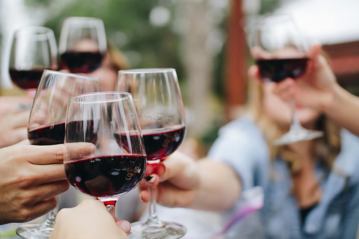 Several people clinking glasses of red wine in a toast, with a blurred outdoor background, evoking the joy and camaraderie often found in Blue Zones, where living longer and healthier lives is part of everyday culture.