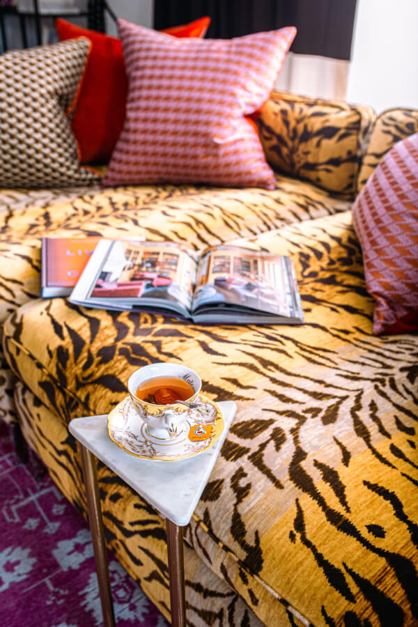 Animal print couch featuring houndstooth throw pillows. Booka re open on the couch and a cup of tea is nearby.