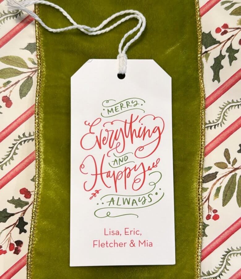 A festive gift tag from Southern Paper Makers with the message "Merry Everything and Happy Always" in red and green script. The background showcases holly and stripes, perfect for adding cheer to your holiday wrap. Names Lisa, Eric, Fletcher, and Mia are at the bottom.