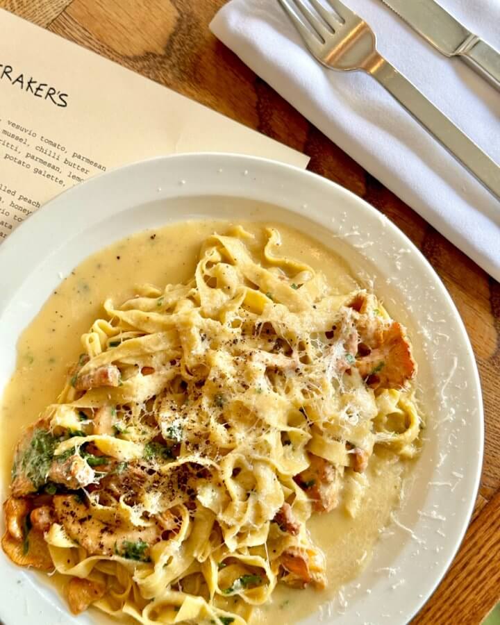 A plate of creamy tagliatelle pasta with mushrooms and grated cheese, served alongside a menu, fork, and knife on a napkin—perfect for indulging in during a long weekend.