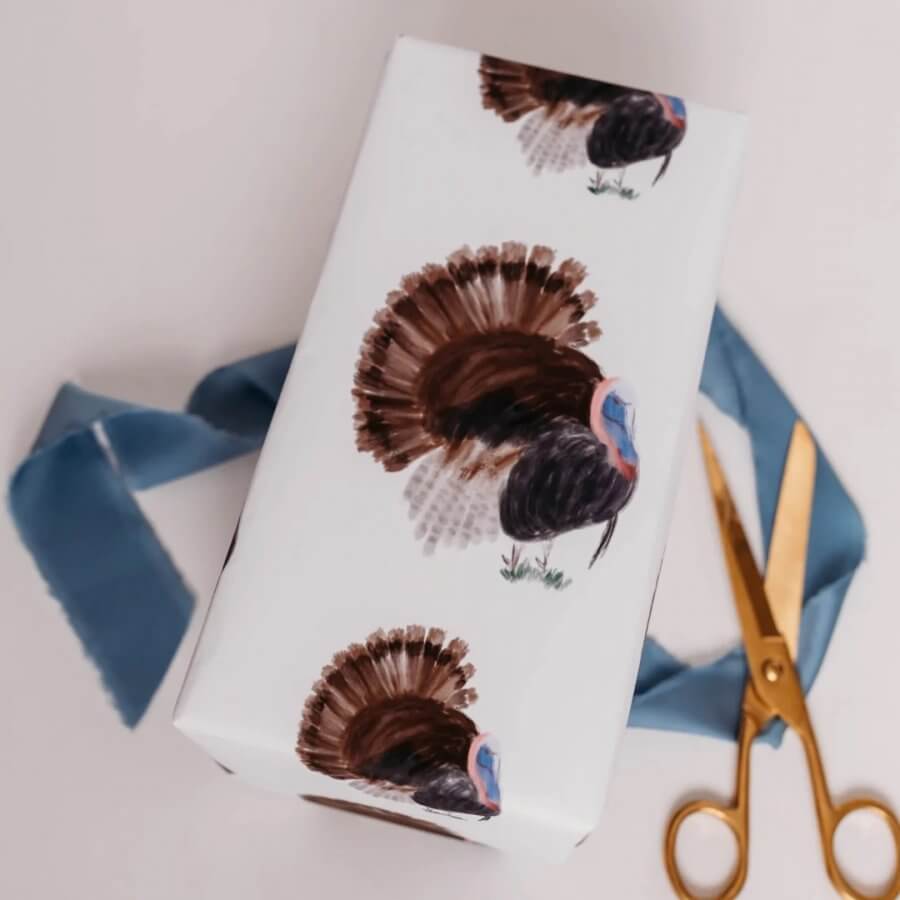 Gift wrap in turkey-themed paper, accompanied by golden scissors and a festive blue ribbon, perfect for the holidays.