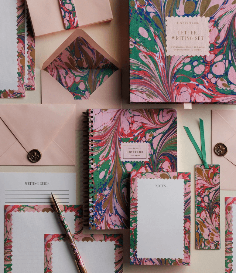 A stationery set features marbled designs and includes a notebook, notepad, envelopes with wax seals, writing paper, and a bookmark. Perfect for the holidays, this elegant collection adds a touch of sophistication to your festive correspondence.