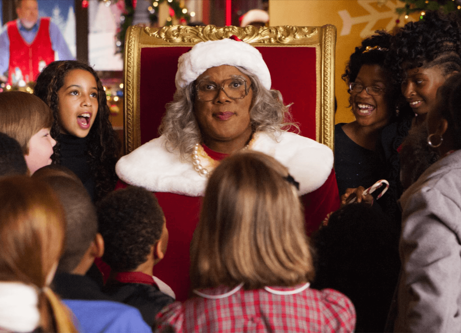 A person dressed as Santa sits on a red chair, surrounded by a group of smiling children, capturing the joyful essence of a holiday scene.