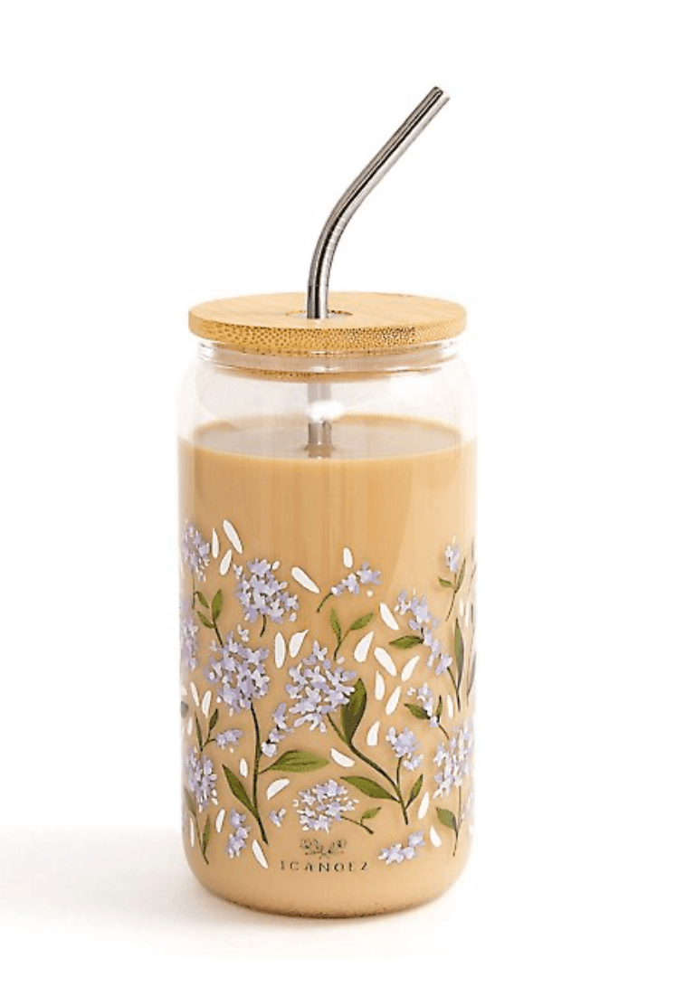 A glass jar with floral patterns brims with a creamy beverage. It features a wooden lid and a sleek metal straw for sipping.