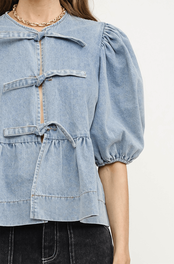 A person dons a denim blouse with puffed sleeves and tied closures, perfectly paired with black jeans.