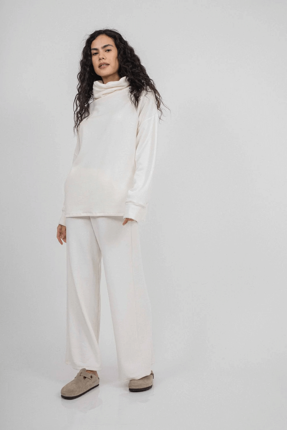 A person in a chic all-white outfit, featuring a high-neck sweater and wide-leg pants, stands against a plain white background. The minimalist style creates the perfect canvas for envisioning New Year’s celebrations or exploring trendy FINDS in vibrant Birmingham.