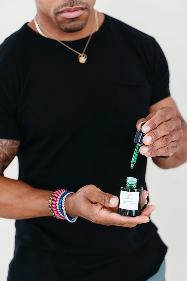 A person in a black shirt holds a small bottle and uses a dropper with green liquid