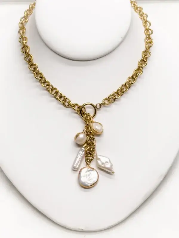 Gold chain necklace with three dangling pearl charms displayed on a white stand.