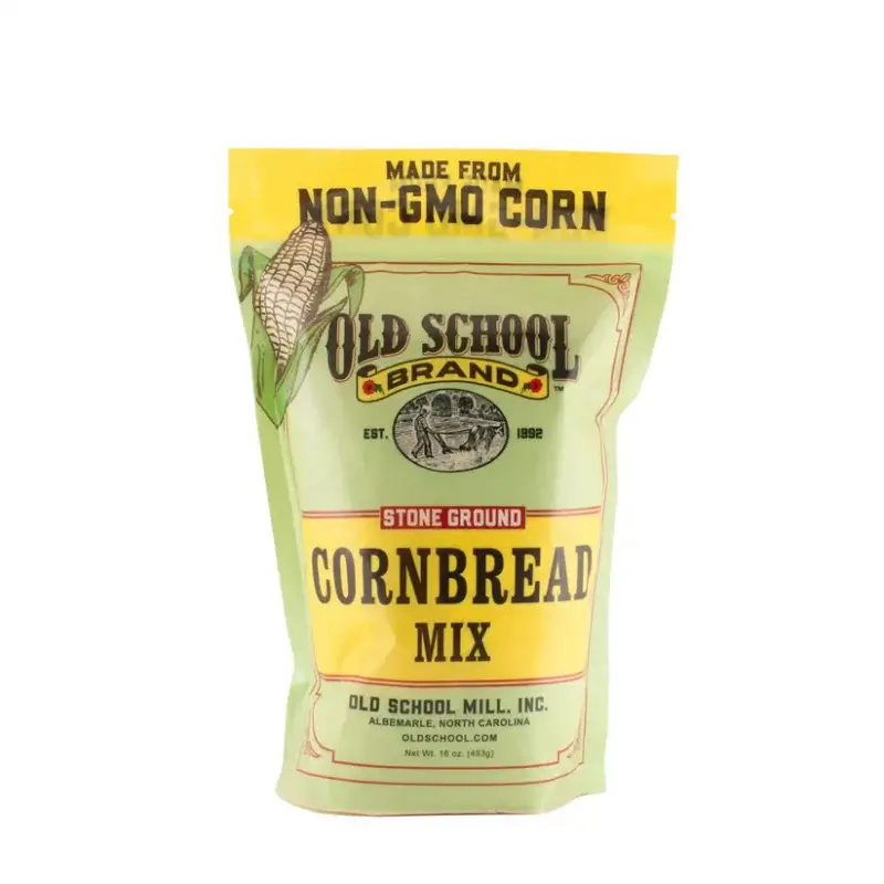 A package of Old School Brand stone ground cornbread mix, made from non-GMO corn, sits in a yellow and green bag adorned with a corn illustration.